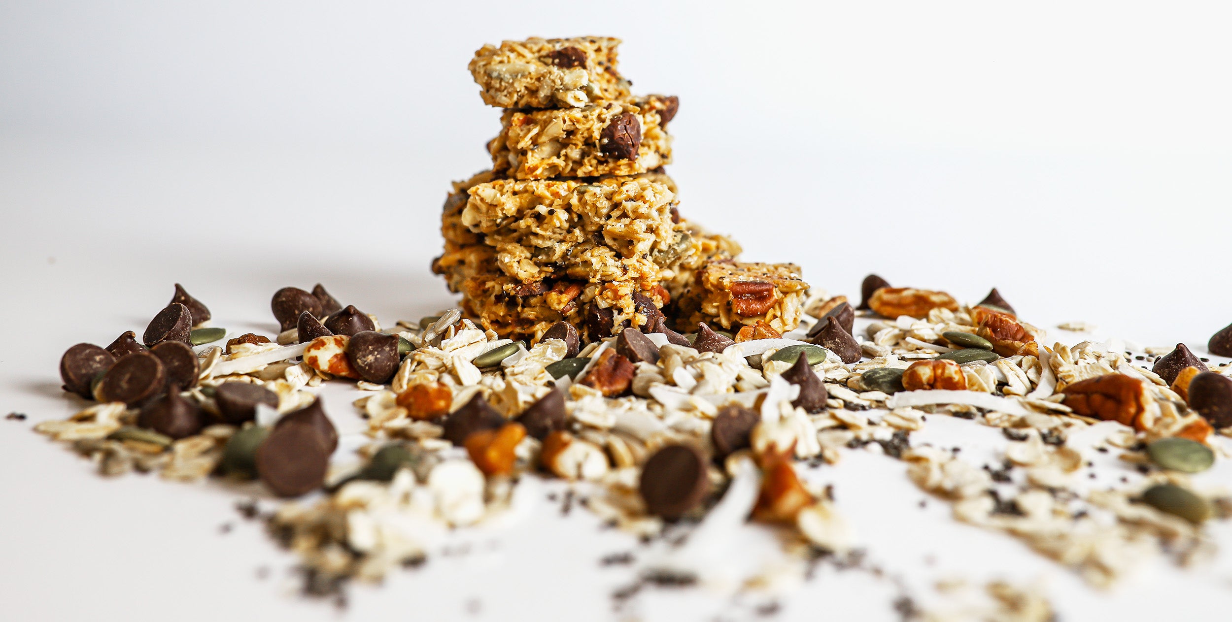 a stack of griff-n-grizzly chocolate chip granola bites surrounded by a scattering of ingredients