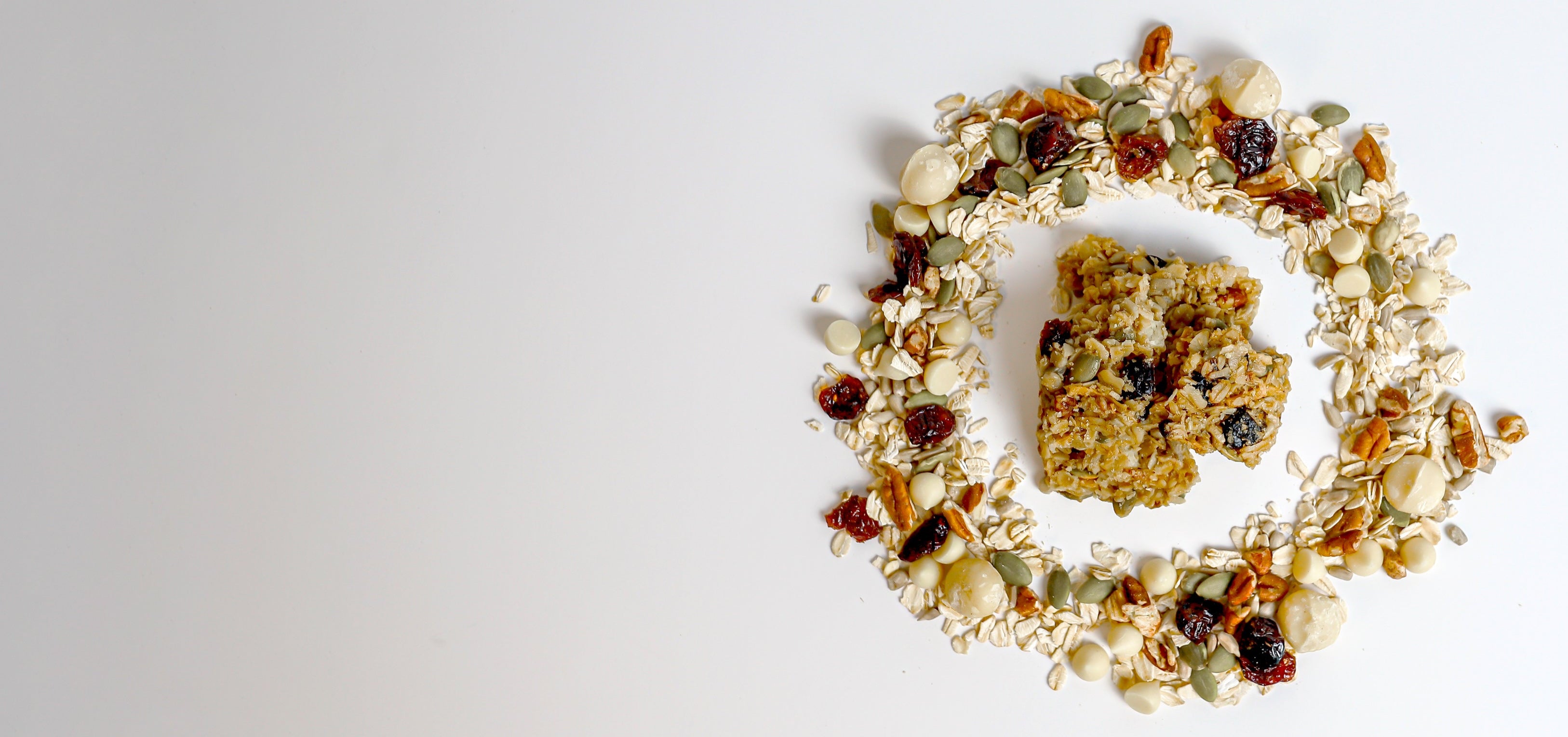 Granola bar surrounded by a wreath of dried fruits and nuts on a white background